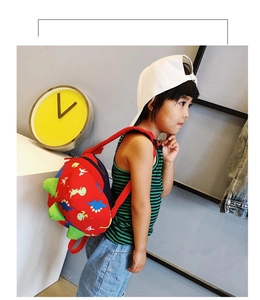 Detail view of a red cartoon dinosaur backpack worn by a child in a cozy indoor setting