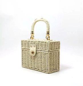 Detail view of woven straw box bag featuring a golden twist lock and beige leather strap