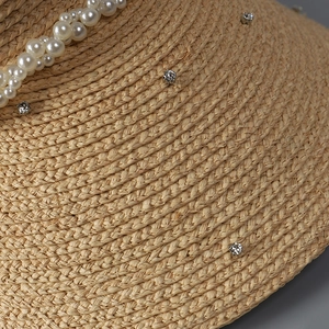 Close-up of woven straw hat featuring elegant white pearls and sparkling rhinestone details