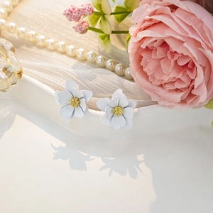 Detail of white flower earrings with yellow stamen near pearls and pink roses
