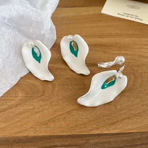 Flat lay of white calla lily jewelry set with green details and pearl accents on wood