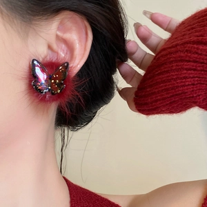 Close-up of butterfly plush earrings with red faux fur balls and iridescent glitter detail