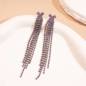 Close-up of geometric purple rhinestone tassel earrings on a white ceramic display tray