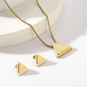 Detail showing gold triangle necklace and earrings set with matte finish on pedestal