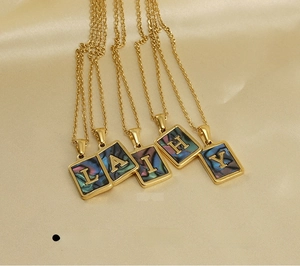 Detailed close-up of shell letter pendants on gold stainless steel chains over silk fabric