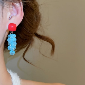 Close-up of square resin grape tassel earring worn by a model in soft warm lighting