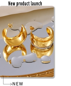 Close-up of golden wide C-shaped hoop earrings on mirror with water droplets