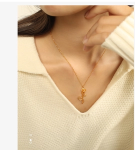 Detailed view of a gold rose pendant necklace on a model wearing a V-neck sweater