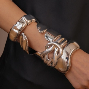 Close-up of stacked silver metal cuffs with textured geometric folds and glossy finish