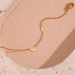 Detail of 18K gold-plated stainless steel chain bracelet with heart charms on beige stone