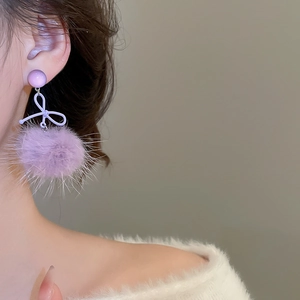 Dettaglio degli orecchini con pompon viola e fiocco indossati da una modella
