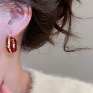 Close-up of deep red resin hoop earring with gold metal band on female model