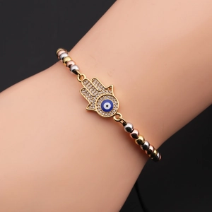 Close-up of gold Hamsa hand and evil eye charm on a tricolor beaded adjustable bracelet