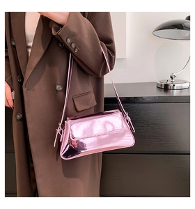 Metallic pink baguette shoulder bag with glossy mirror finish shown on a woman in a coat