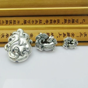 Three vintage silver nine-tailed fox pendants in various sizes on a traditional scroll