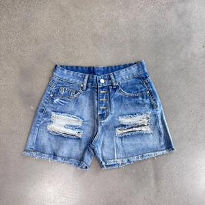 Detail of high waisted blue denim shorts with distressed rips and frayed tassel hem