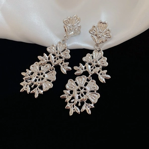 Detail shot of cascading hollow silver flower earrings on elegant black and white silk
