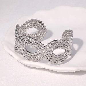 Polished silver stainless steel open bangle featuring a woven infinity knot design on a tray