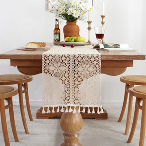 Beige crochet table runner with tassels and hollow floral design on a wooden table
