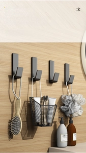 Detail of four matte black J-shaped adhesive wall hooks on a light wood grain surface