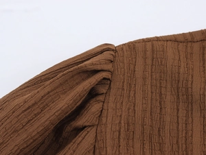 Detail of brown pleated fabric showing fine stitching on the shoulder and sleeve