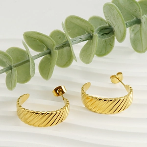 Close-up of 18K gold-plated twisted C-shape hoop earrings on a white wavy background