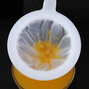 Fine mesh soy milk and juice strainer bag with handle filtering pulp over a glass cup