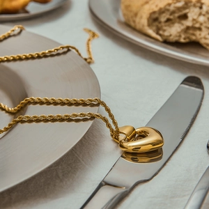 Détail d'un collier pendentif cœur doré posé sur un couteau dans un décor de repas