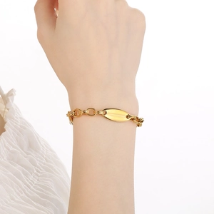 Detail eines goldfarbenen Gliederkettenarmbands mit mattiertem ovalem Metallanhänger am Handgelenk