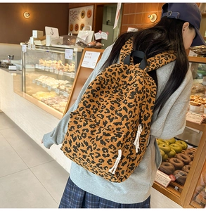 Detail view of leopard print corduroy backpack with retro rope zippers in a warm cafe setting