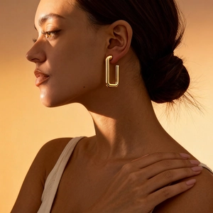 Minimalist gold rectangular paperclip earring worn by a model in warm soft lighting