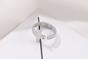 Close-up of a silver cross-shaped open ring on a geometric stand with a textured background