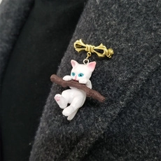 Detail of creative white cat brooch pinned on dark grey tweed coat lapel with gold pin