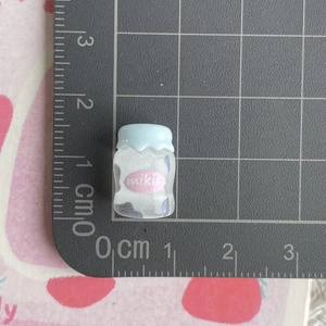 Miniature juice bottle charm with blue lid and glitter on a measuring mat