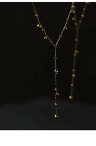 Macro detail of the 18k gold-plated Y-shaped necklace with polished beads on dark background