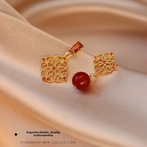 Close-up of hollowed-out flower earrings with red beads on champagne silk background
