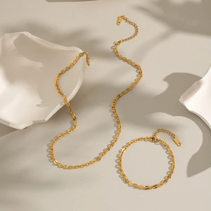Ensemble collier et bracelet à chaîne dorée minimaliste sur une surface grise