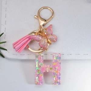 Close-up of resin letter H keychain with pink butterfly sequins and suede tassel detail