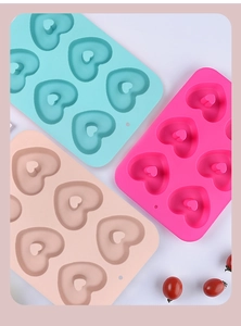 Three heart-shaped silicone molds in pink, blue, and beige with cherry accents