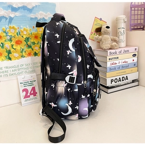 Side view of black backpack with moon and star print on a desk in a cozy lifestyle setting