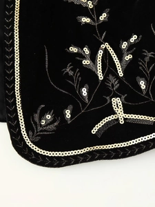 Detailed close-up of golden embroidery and sequins on black velvet vest fabric