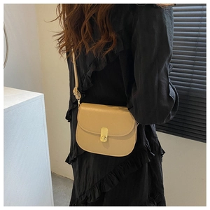 Macro shot of light khaki leather saddle bag with gold metal buckle on female model