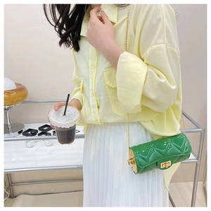 Detail of green quilted cylindrical bag with golden chain strap on a model's outfit