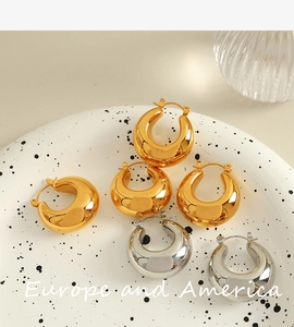 Detailed view of thick hollow gold and silver hoop earrings on a ceramic plate