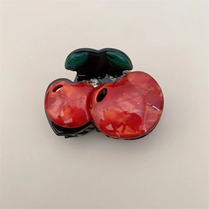 Detail of red cherry hair claw clip showing glossy acetate texture and green leaf design