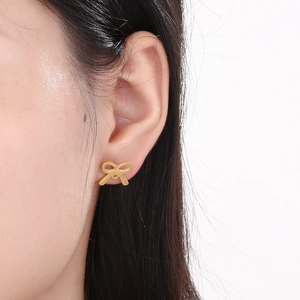Close-up of minimalist gold bow-shaped titanium steel stud earrings worn on ear