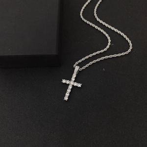 Close-up of silver cross pendant with clear rhinestones on rope chain over dark texture