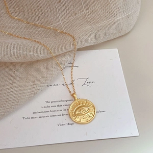 Detailed view of an 18K gold plated evil eye pendant on a fine link chain with sunburst relief