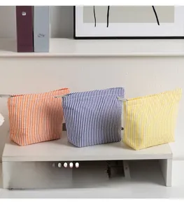 Three striped seersucker makeup bags in orange, blue, and yellow on a white shelf