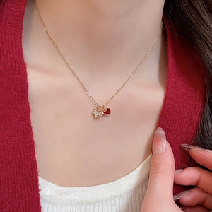 Gros plan d'un collier doré avec un pendentif cœur rouge et un papillon en zircon scintillant